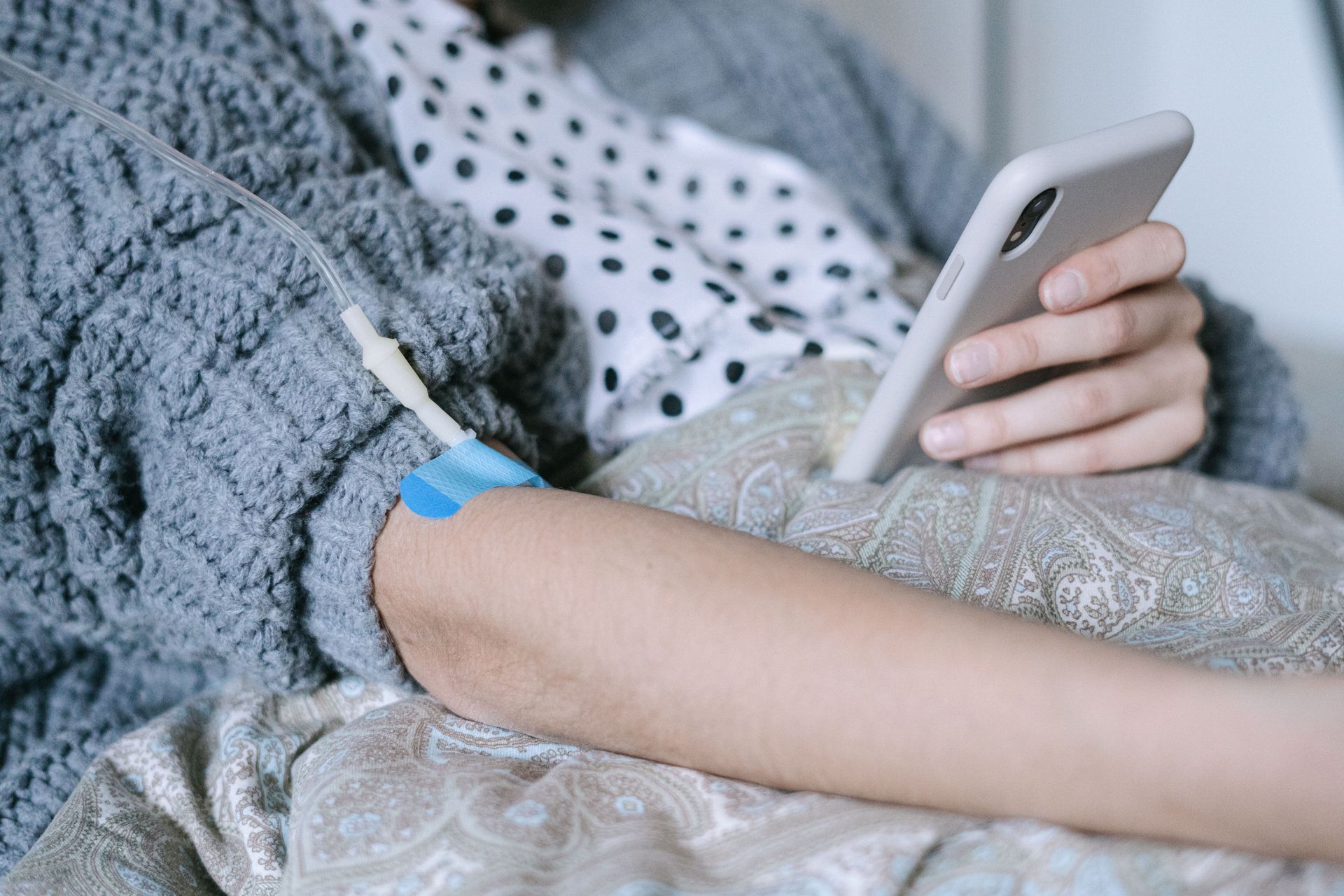 A woman receiving intravenous therapy for cancer treatment while using her phone, symbolizing connection and hope.