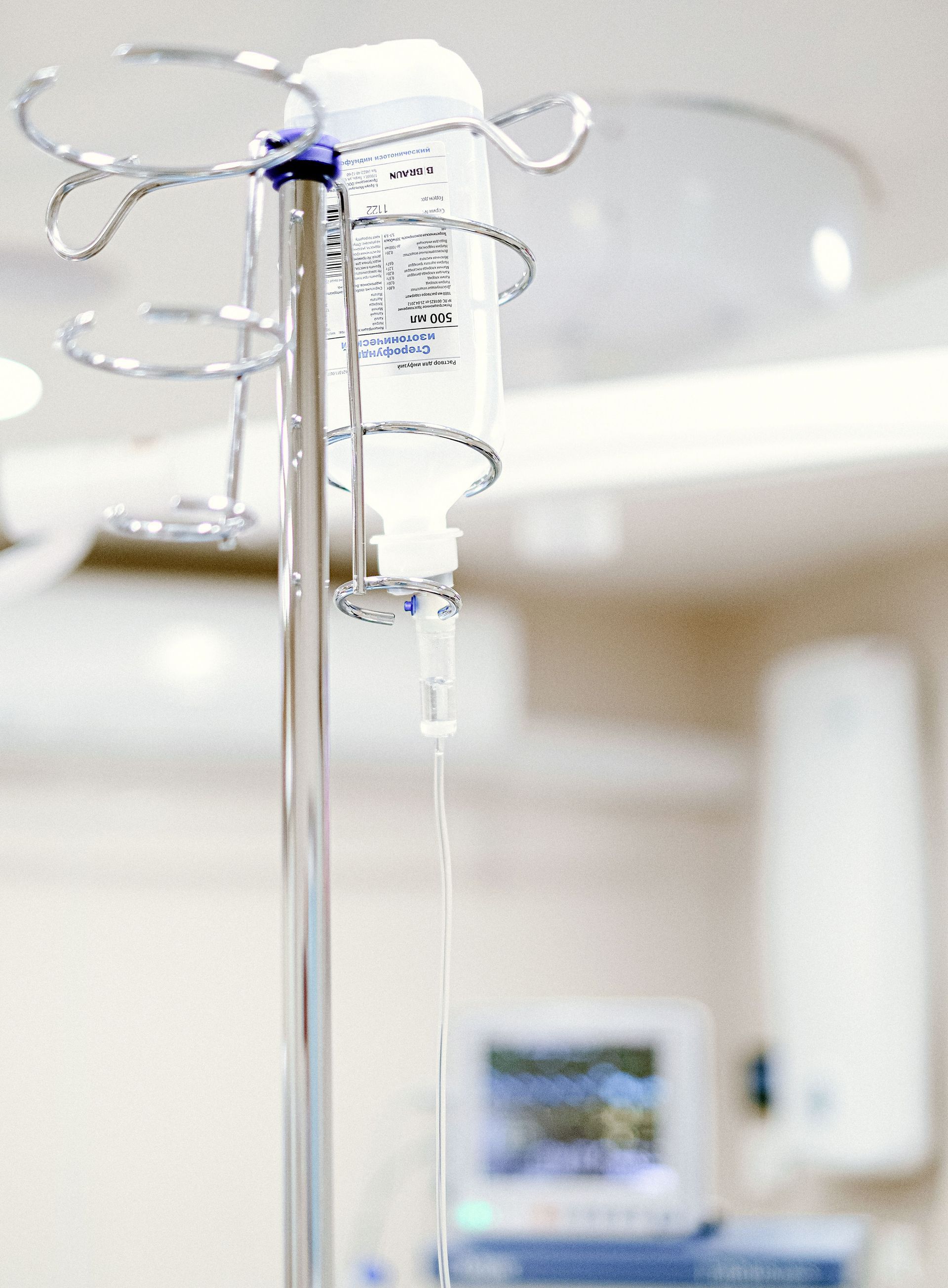 Close-up of an IV drip in a sterile hospital setting with background medical equipment.