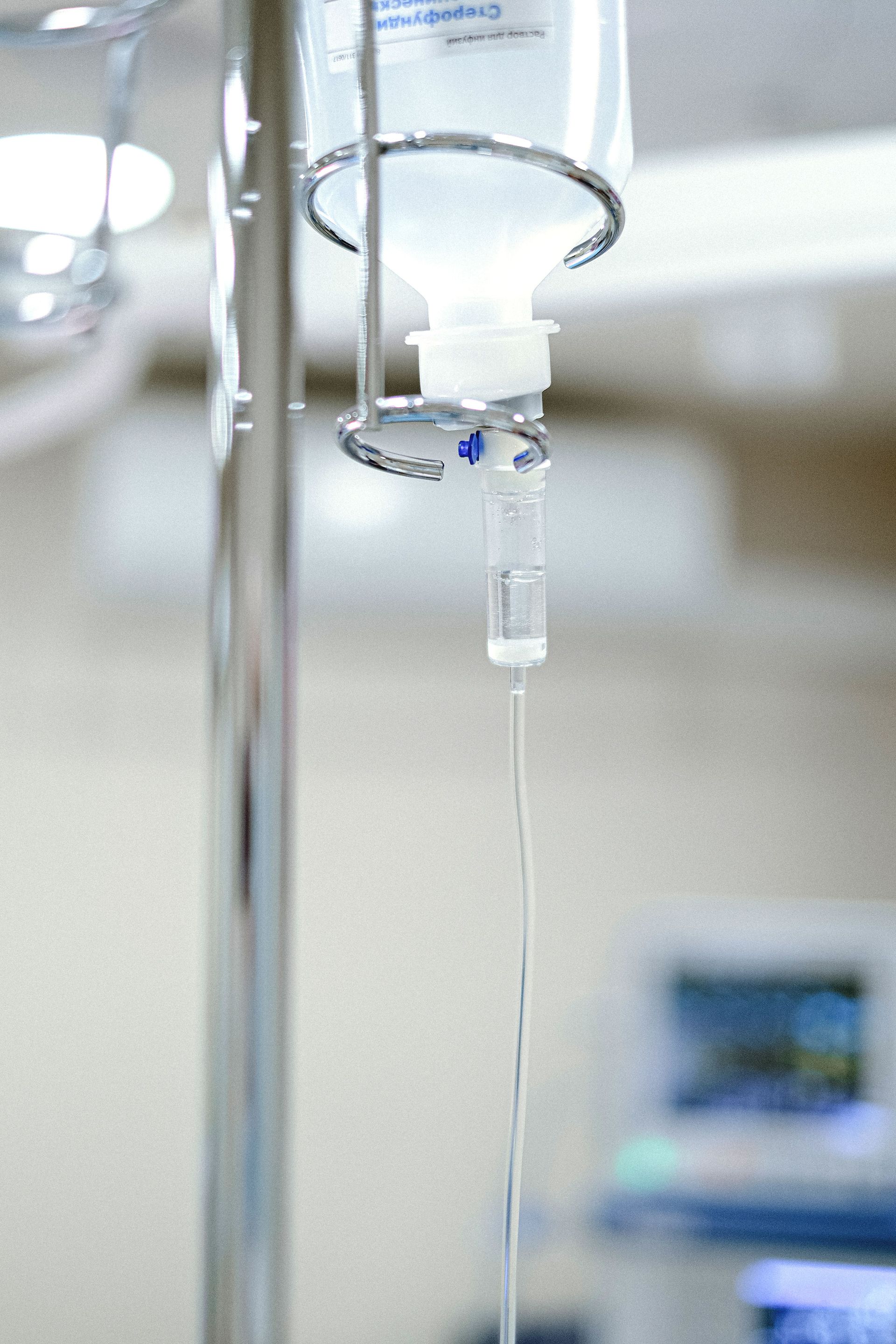Close-up view of an IV drip chamber and stand in a clinical hospital environment.